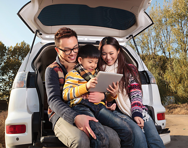 Parents and son sitting in trunk of car looking at tablet